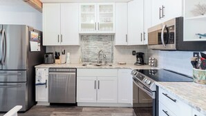 Een moderne keuken met witte kasten, roestvrijstalen apparatuur en een betegelde achterwand.