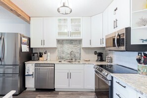 A modern kitchen with white cabinets, stainless steel appliances, and a stone backsplash.