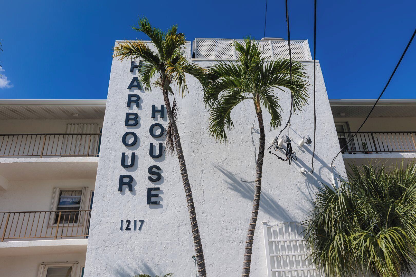 Un bâtiment sur lequel on peut lire l’inscription « HARBOUR HOUSE 1217 », avec deux palmiers devant.