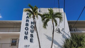 Een gebouw met een bord waarop 'HARBOUR HOUSE 1217' staat, en twee palmbomen ervoor.