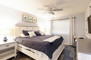 A bedroom with a bed, bedside tables, a ceiling fan, a window with curtains, and a TV stand.
