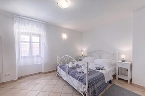 Ein Schlafzimmer mit einem Bett, Nachttischen, einem Fenster mit Vorhängen und einer Deckenleuchte.