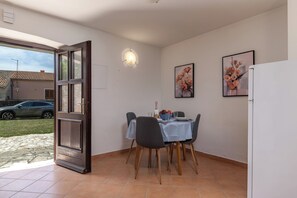 A dining area with a table set for two, a refrigerator, and a door leading outside.
