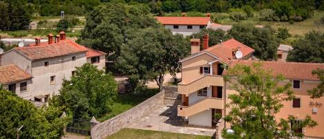 A residential area with houses featuring red-tiled roofs and stone walls, surrounded by greenery and trees.