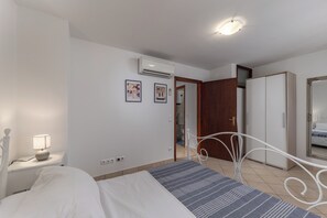 A bedroom with a bed, bedside lamp, air conditioning unit, wardrobe, and a mirror.