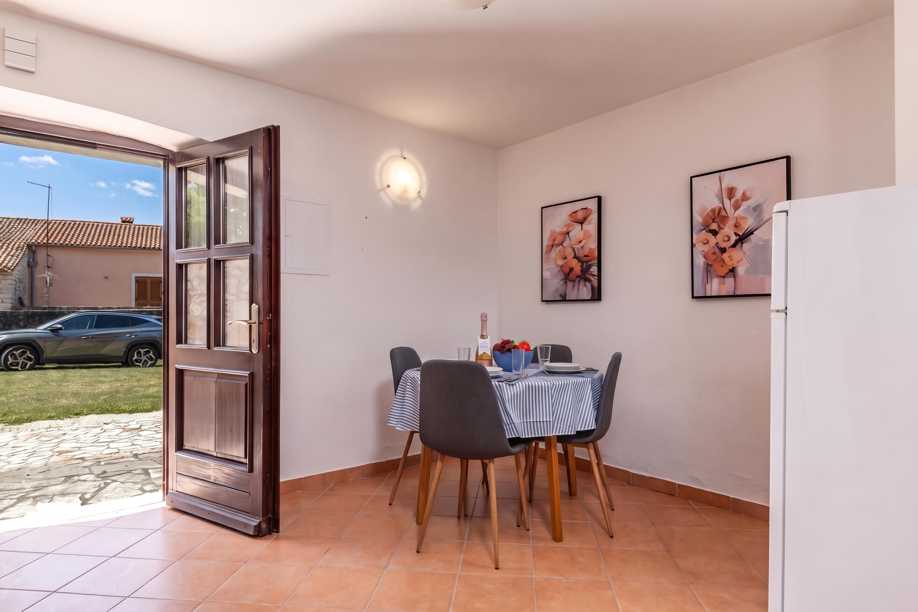 A dining area with a table set for two, a refrigerator, and a door leading outside.