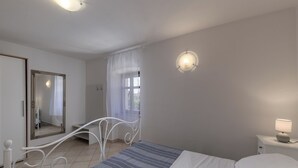 A bedroom with a bed, a bedside table with a lamp, a window with curtains, a mirror, and a door. - Istrian Countryside House Iva, Rovinj-Krmed, Croatia (Krmed)
