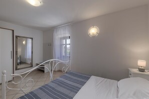 A bedroom with a bed, a bedside table with a lamp, a window with curtains, a mirror, and a door. - Villa Iva, Krmed, Croatia (Krmed)
