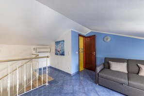 A staircase with white balusters, a grey sofa with cushions, and a blue tiled floor.