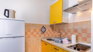Une cuisine avec un réfrigérateur blanc, des placards jaunes, un évier et un mur recouvert de carreaux.