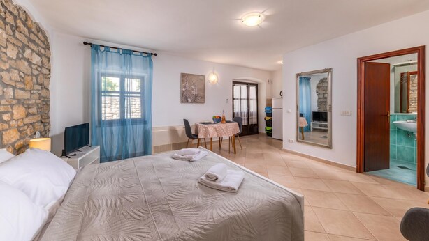 Une chambre à coucher comprenant un lit, un bureau, une chaise, une table et une salle de bain visible à travers une porte ouverte.
