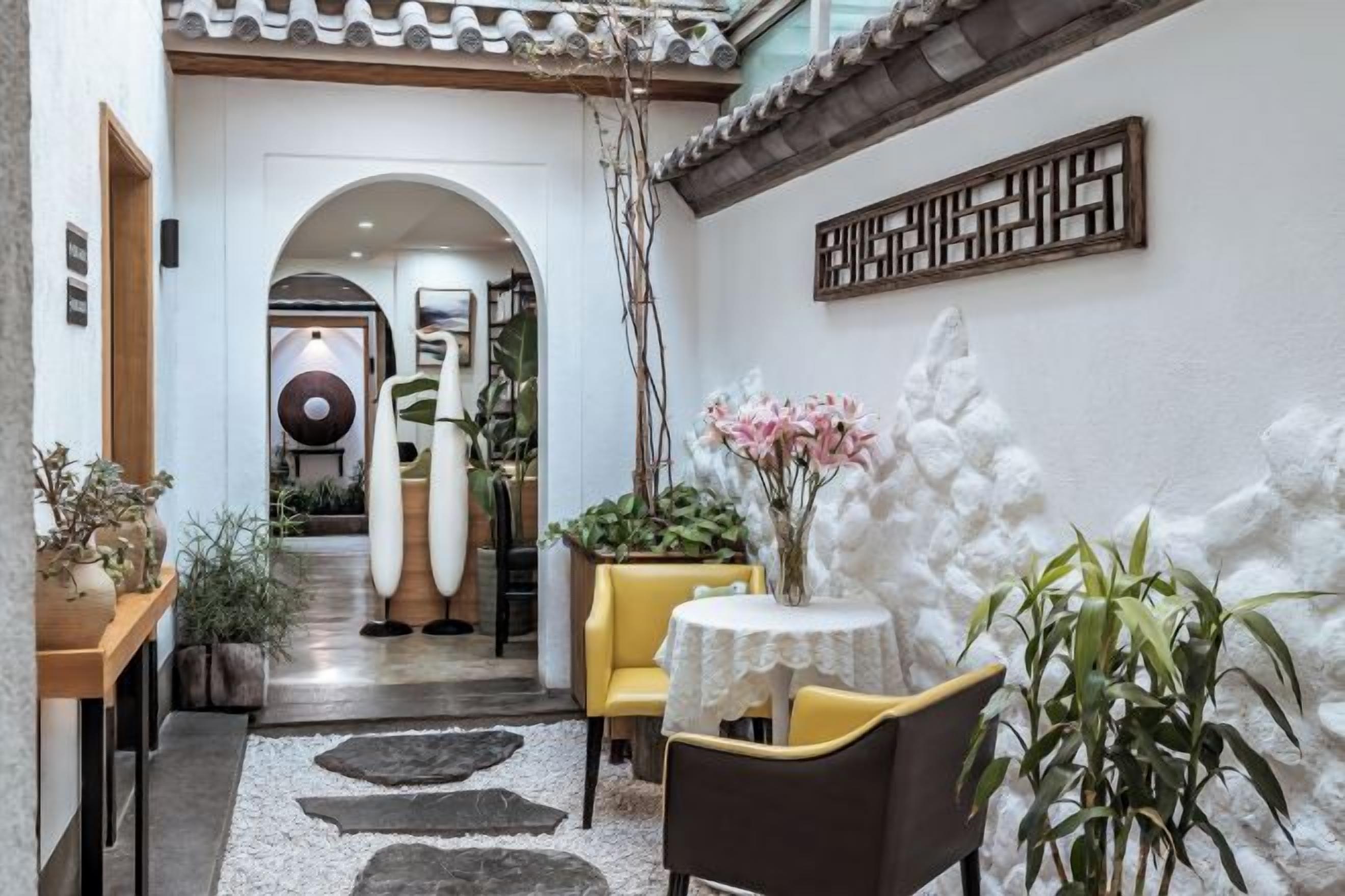 A hotel lobby with a reception desk, a dining area with a table and chairs, and a decorative wall.