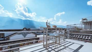 A rooftop terrace with a view of mountains, a pergola, and a dining area.