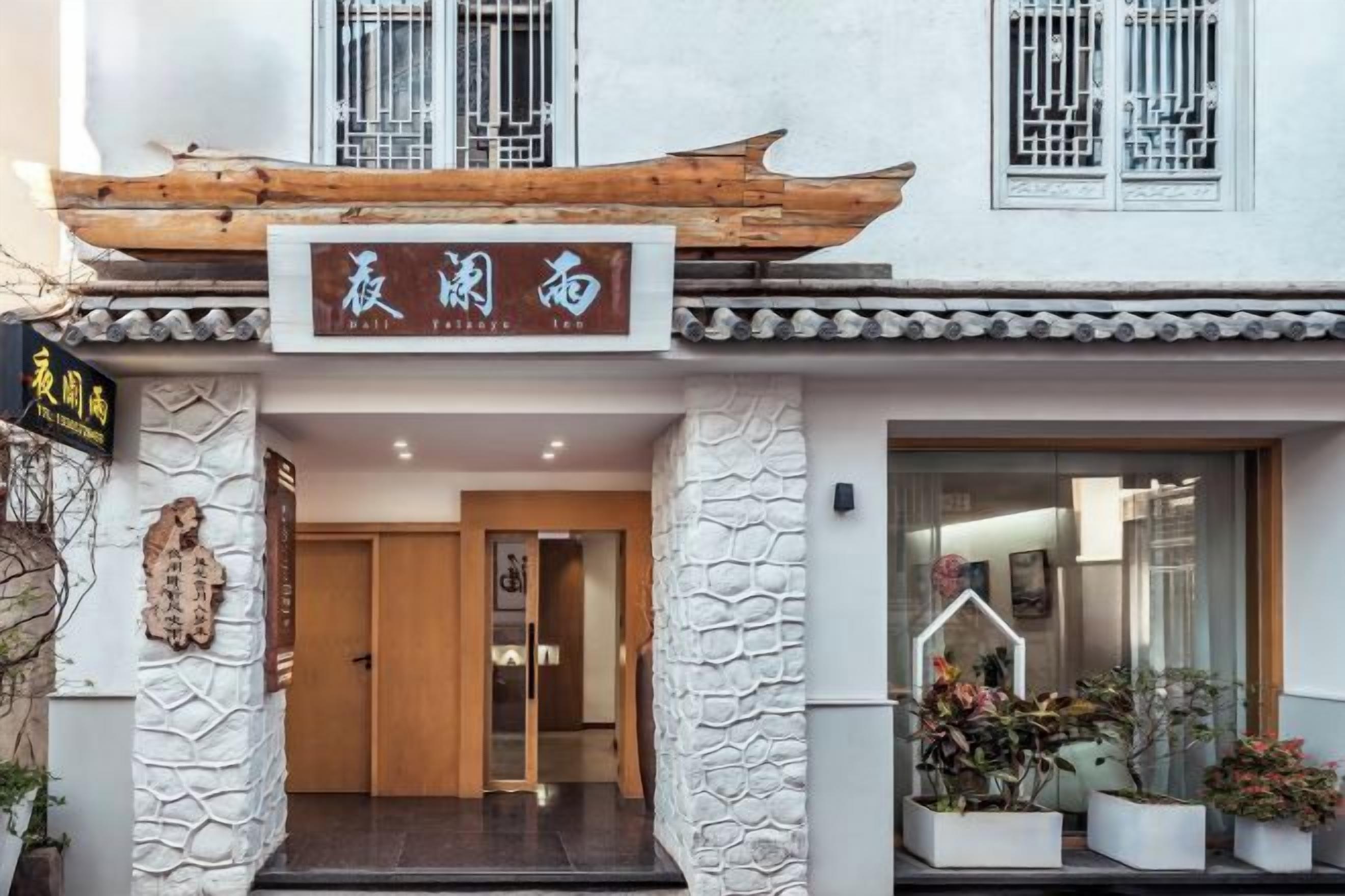 A traditional building with a signboard, a wooden structure above the entrance, and potted plants outside.
