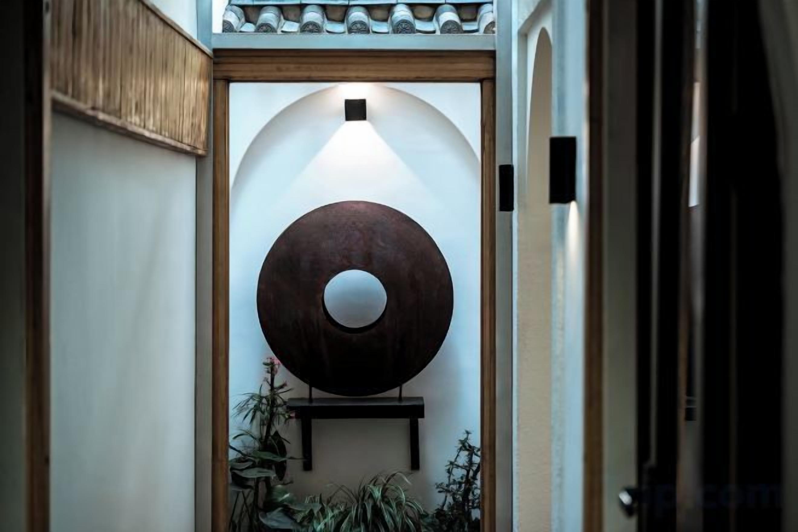 A hallway with a large circular wall art piece, a wooden door frame, and a small shelf with plants.