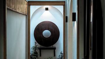 A hallway with a large circular wall art piece, a wooden door frame, and a small shelf with plants.