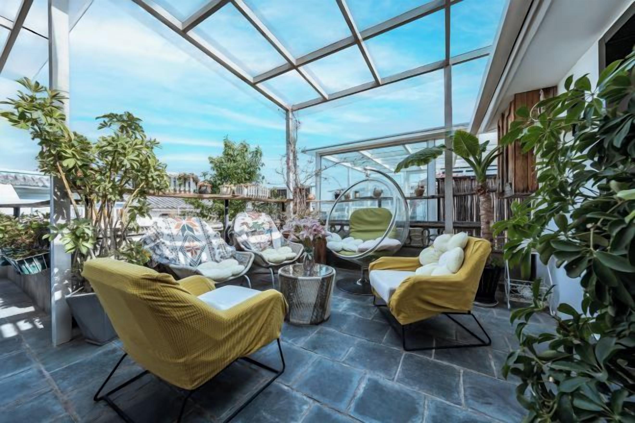 A glass-enclosed patio with seating, plants, and a view of the city.