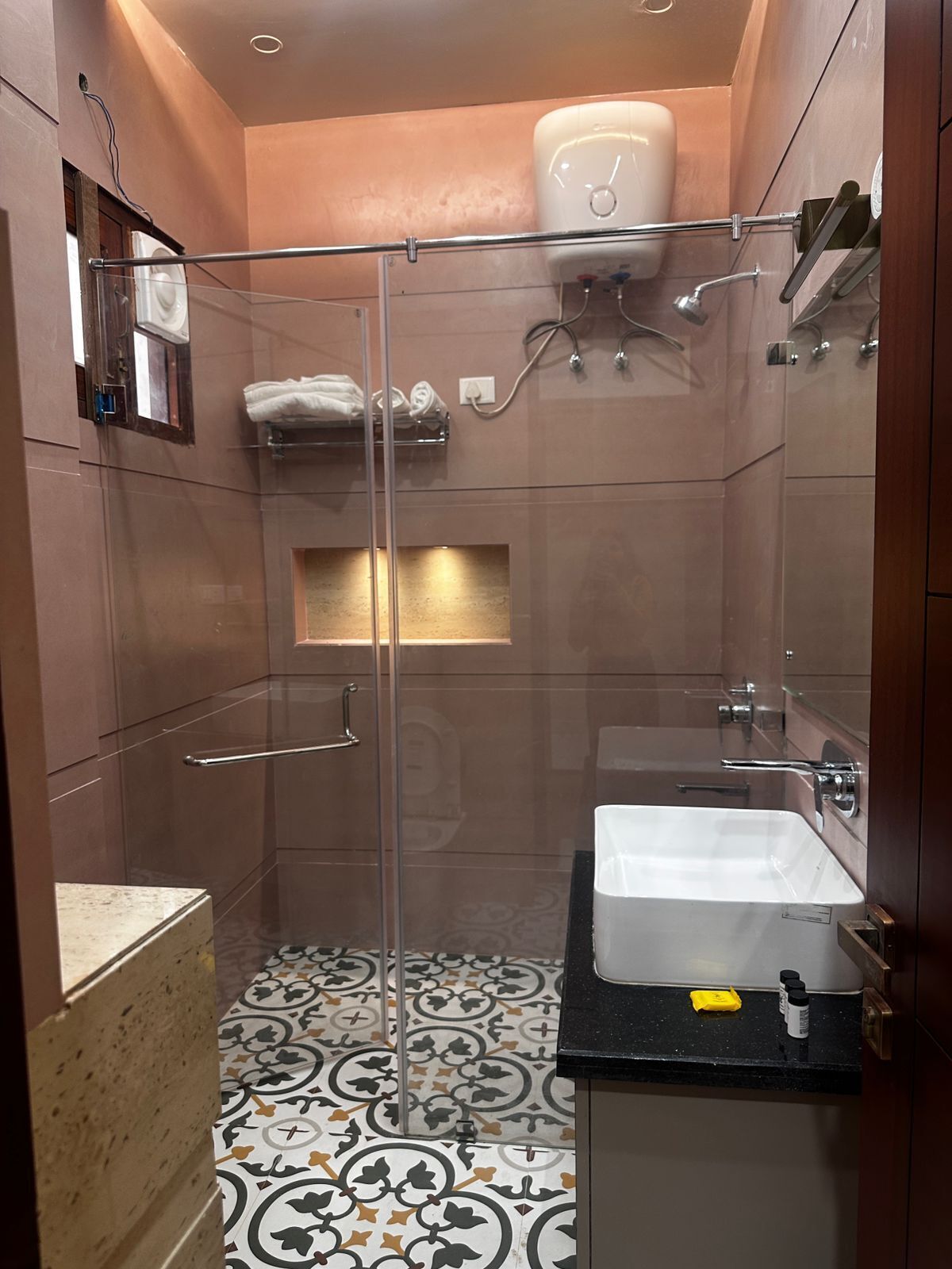 A modern bathroom with a glass-enclosed shower, a white sink, and a patterned floor.