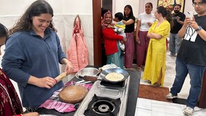 A group of people gathered around a kitchen area with a stove, cooking utensils, and a bread loaf. - Beautiful Homestay (Agra)