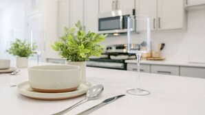 Une cuisine moderne avec des meubles blancs, un four à micro-ondes et une table à manger agrémentée d’un bol, d’une cuillère et d’un verre.