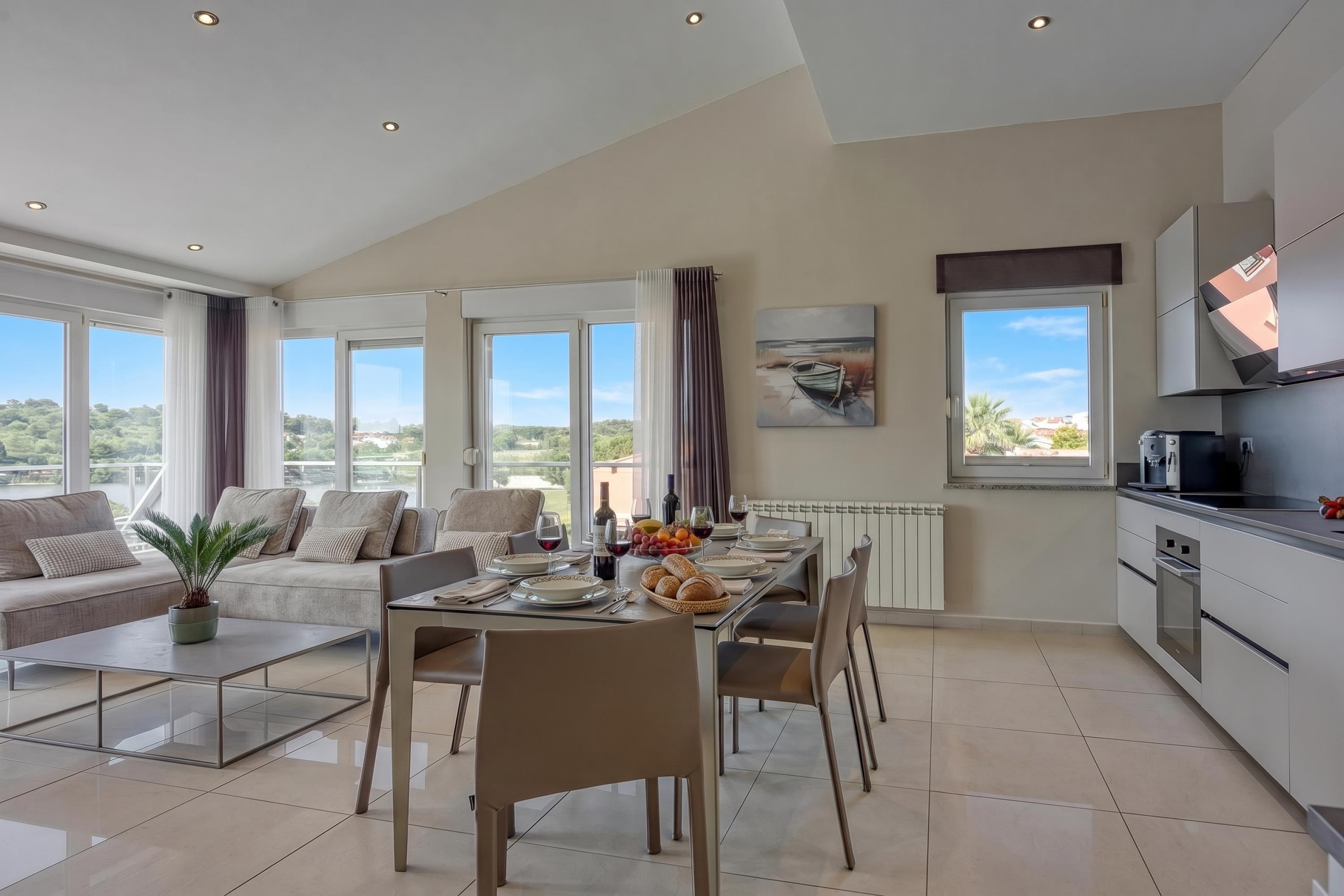 A modern living space with a dining area, kitchen, and large windows offering views of the outdoors.