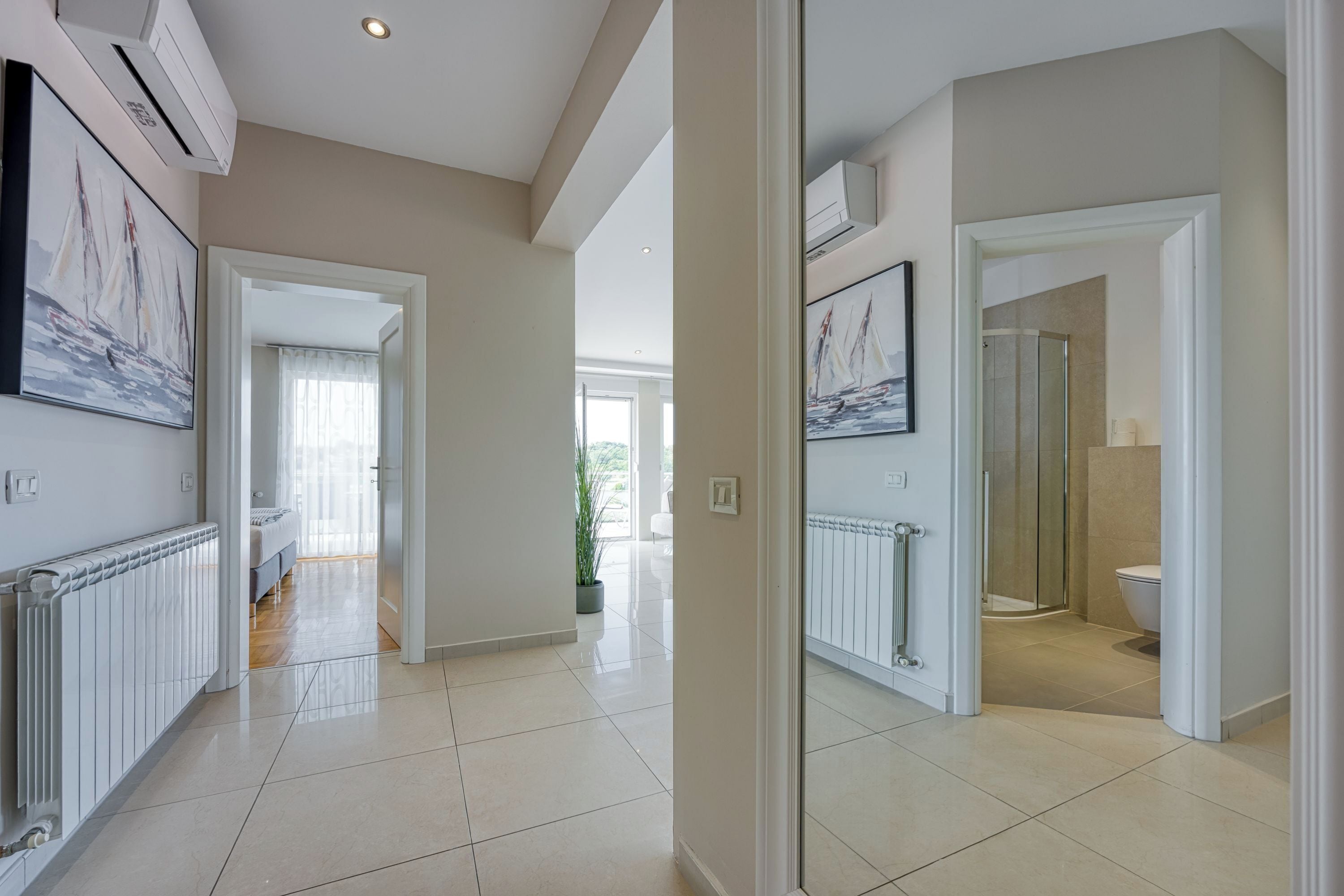 A modern interior with a hallway leading to a bedroom, a bathroom with a shower, and a dining area with a table and chairs.