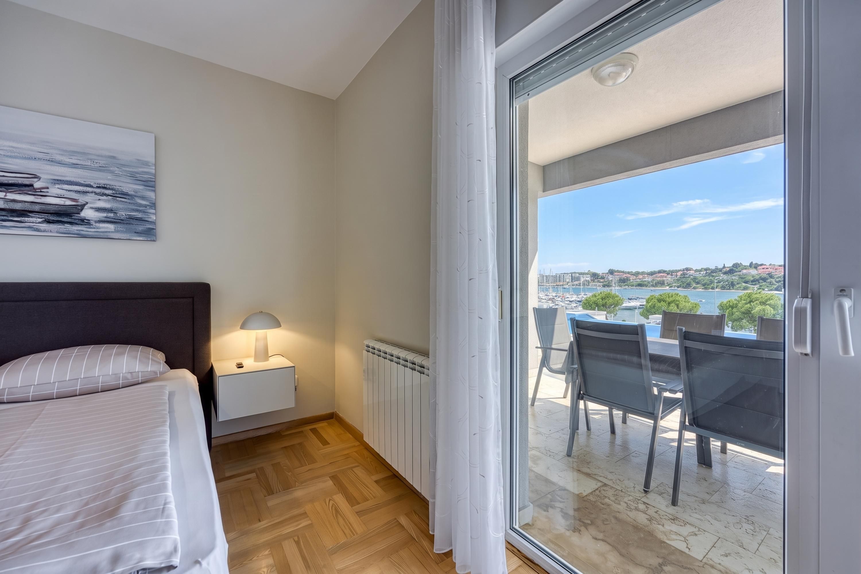 Ein Schlafzimmer mit Bett, Nachttisch, Lampe und Blick auf eine Marina durch eine Schiebetür.
