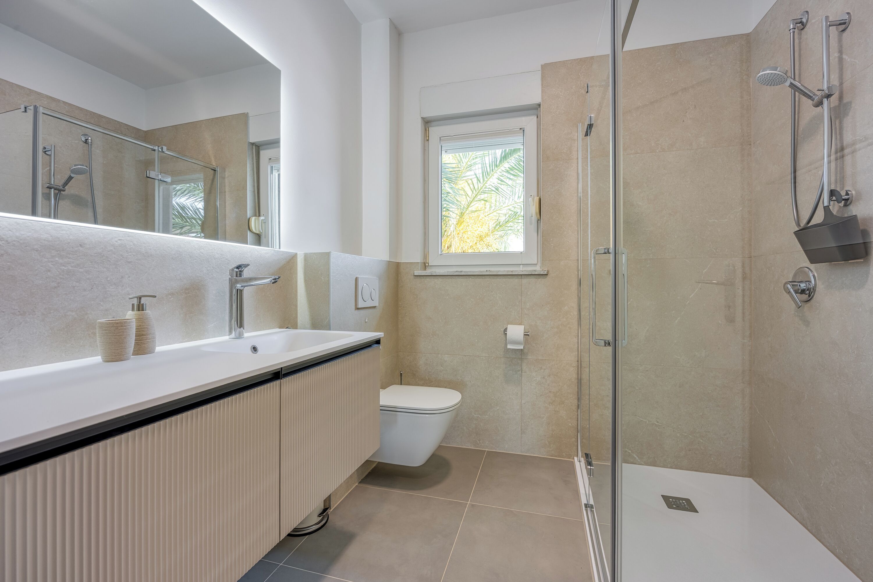Un baño moderno con ducha de vidrio, inodoro y lavamanos con espejo.