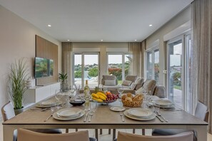 A dining area with a table set for six, a fruit bowl, and a bottle of wine. - Elegant Panoramic Seaview Apartment 2, Pula, Croatia (Pula)