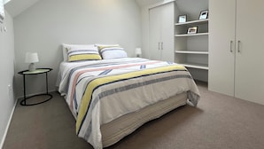 Une chambre dotée d’une lucarne, d’un lit avec une literie à rayures, d’une table de chevet avec une lampe et d’étagères intégrées.