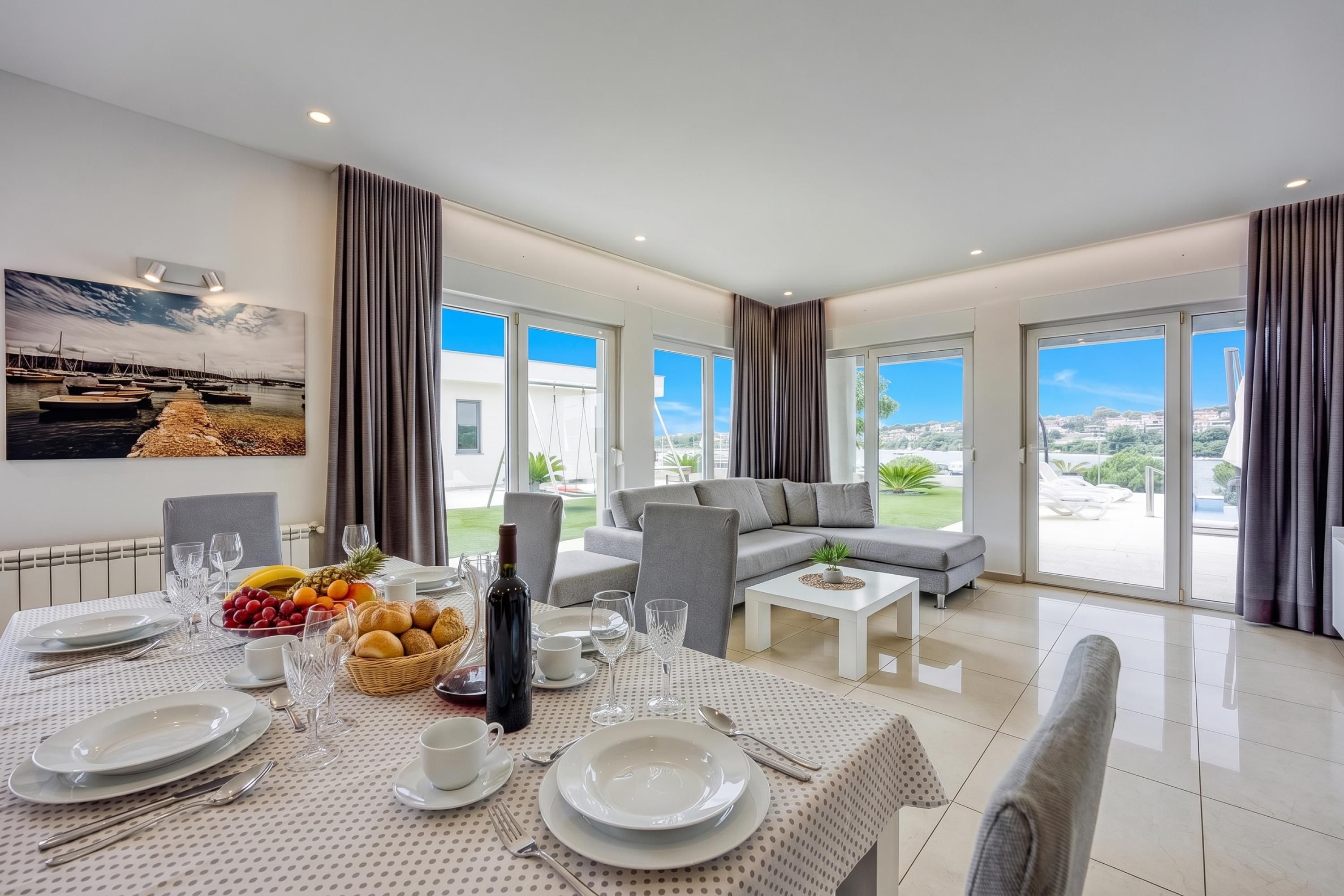 A modern living room with a dining area, large windows, and a view of the landscape.