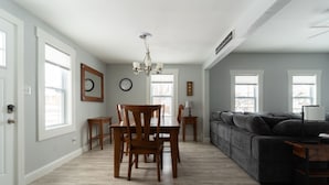 Amplia sala de estar con un sofá de color gris oscuro, una mesa de comedor de madera y sillas, y una araña.