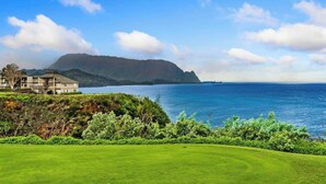 Une vue sur la côte, avec un terrain de golf, un grand bâtiment à plusieurs étages et une montagne en arrière-plan.