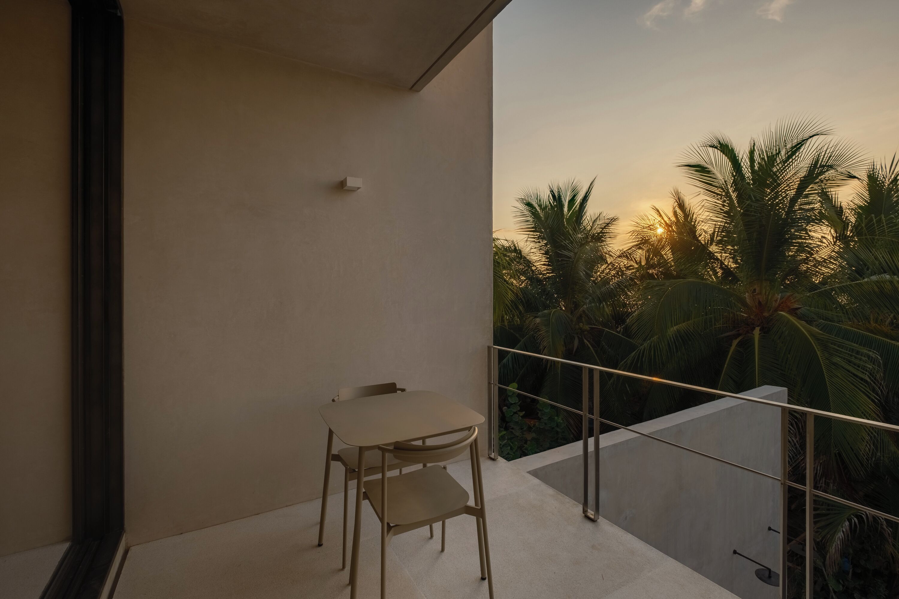 Ein Balkon mit Tisch und Stühlen, mit Blick auf Palmen und einen Sonnenuntergang.