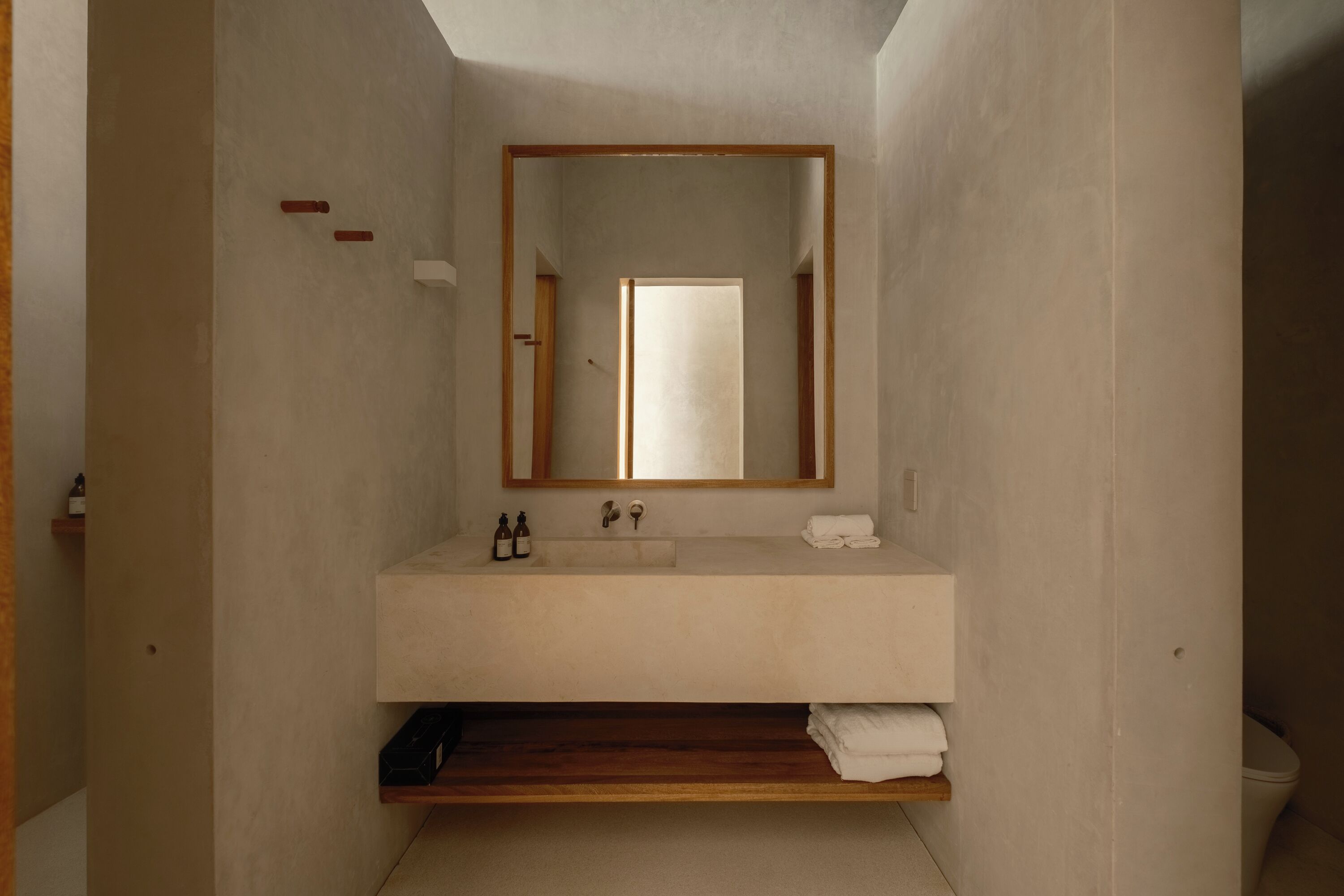 A minimalist bathroom with a wooden shelf, a white sink, and a mirror.