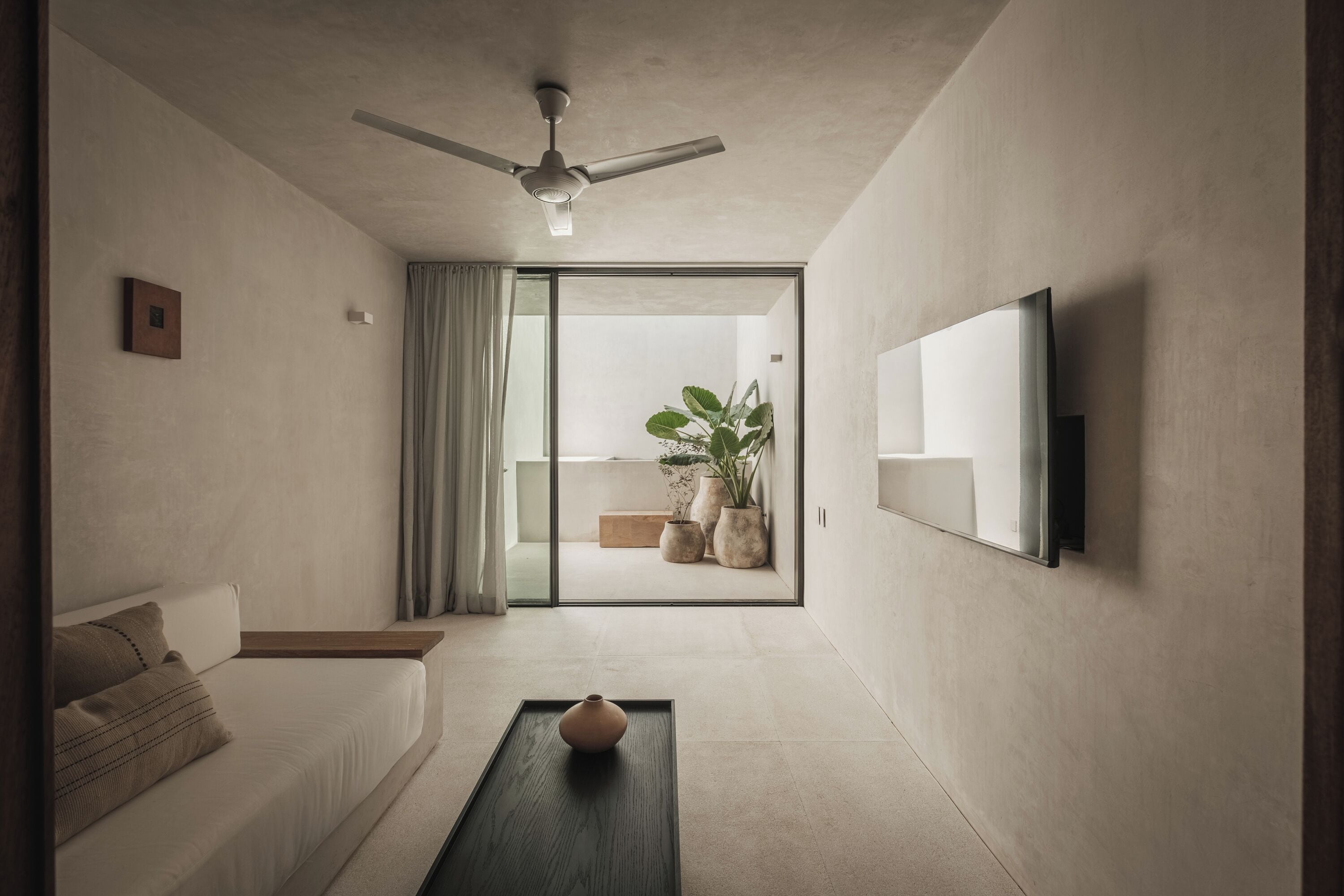 A modern living room with a sofa, a coffee table, a ceiling fan, and a large window with curtains.