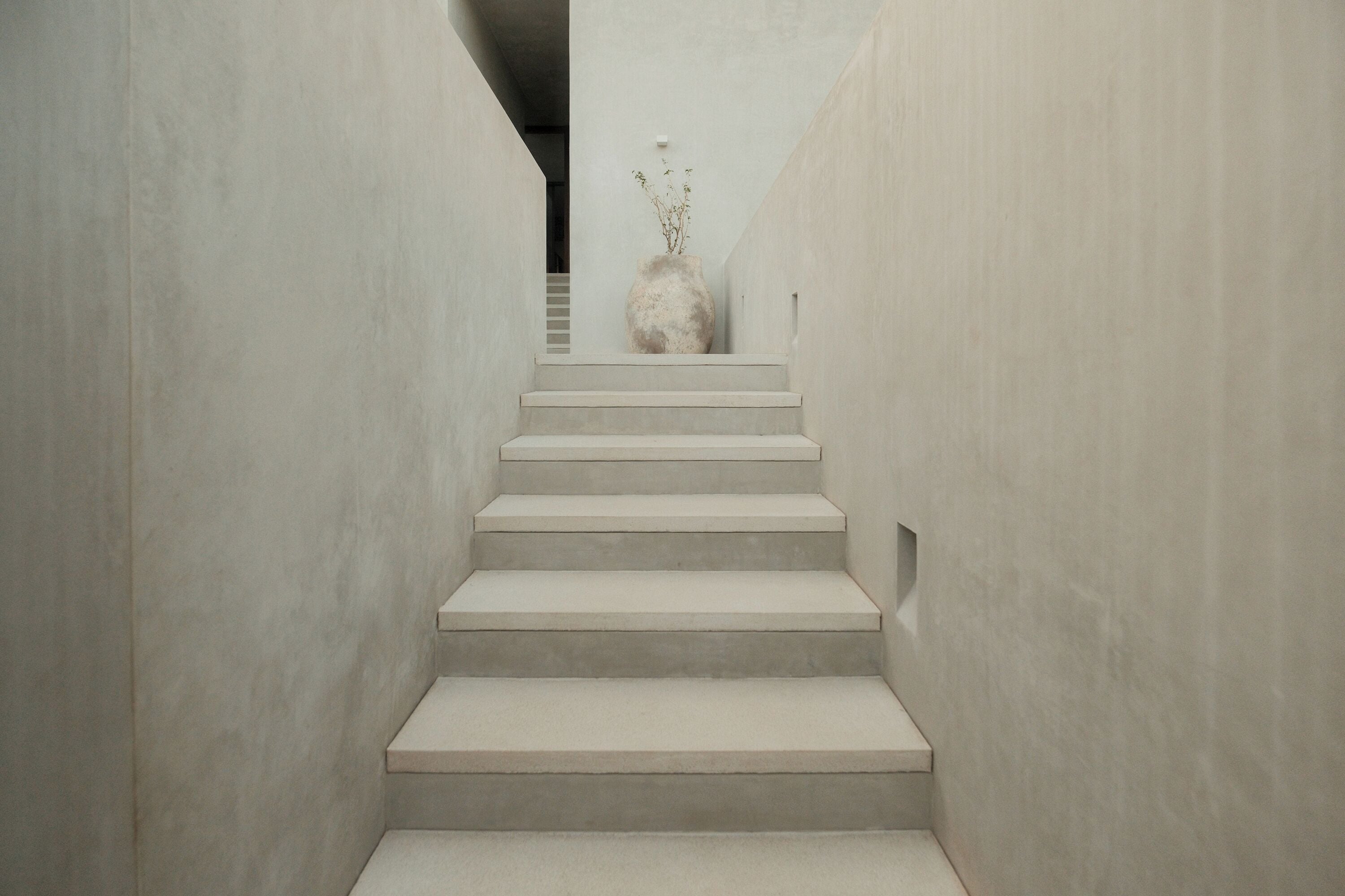 A staircase leading to a landing with a large vase of dried plants.