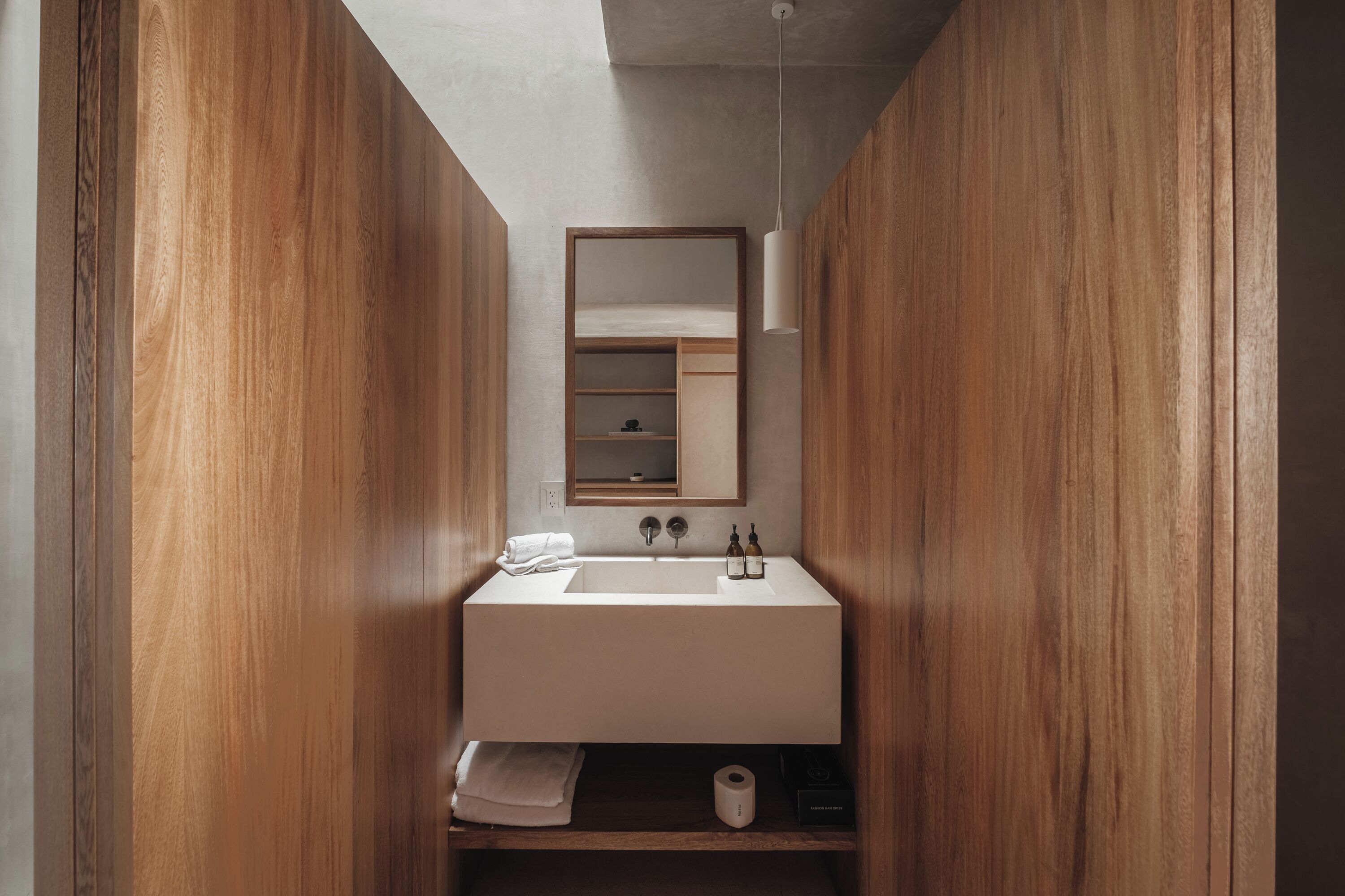 Un bagno compatto con un mobile bagno in legno, un lavandino bianco, uno specchio e uno scaffale con articoli da toilette.