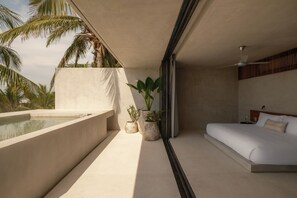 A modern bedroom with a large bed, a small balcony with a pool, and potted plants. - Notto Zicatela Hotel (Puerto Escondido)