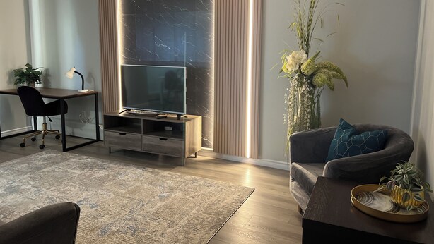 Una sala de estar moderna con una televisión de pantalla plana, un escritorio, un sofá cómodo y una planta decorativa.
