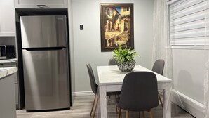 Una cocina moderna con un refrigerador de acero inoxidable, una mesa de comedor con sillas y una planta en maceta.