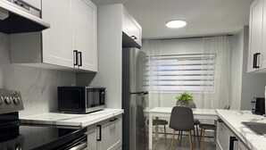 Una cocina moderna con armarios blancos, un microondas negro, un refrigerador de acero inoxidable y una zona de comedor con una mesa y sillas.