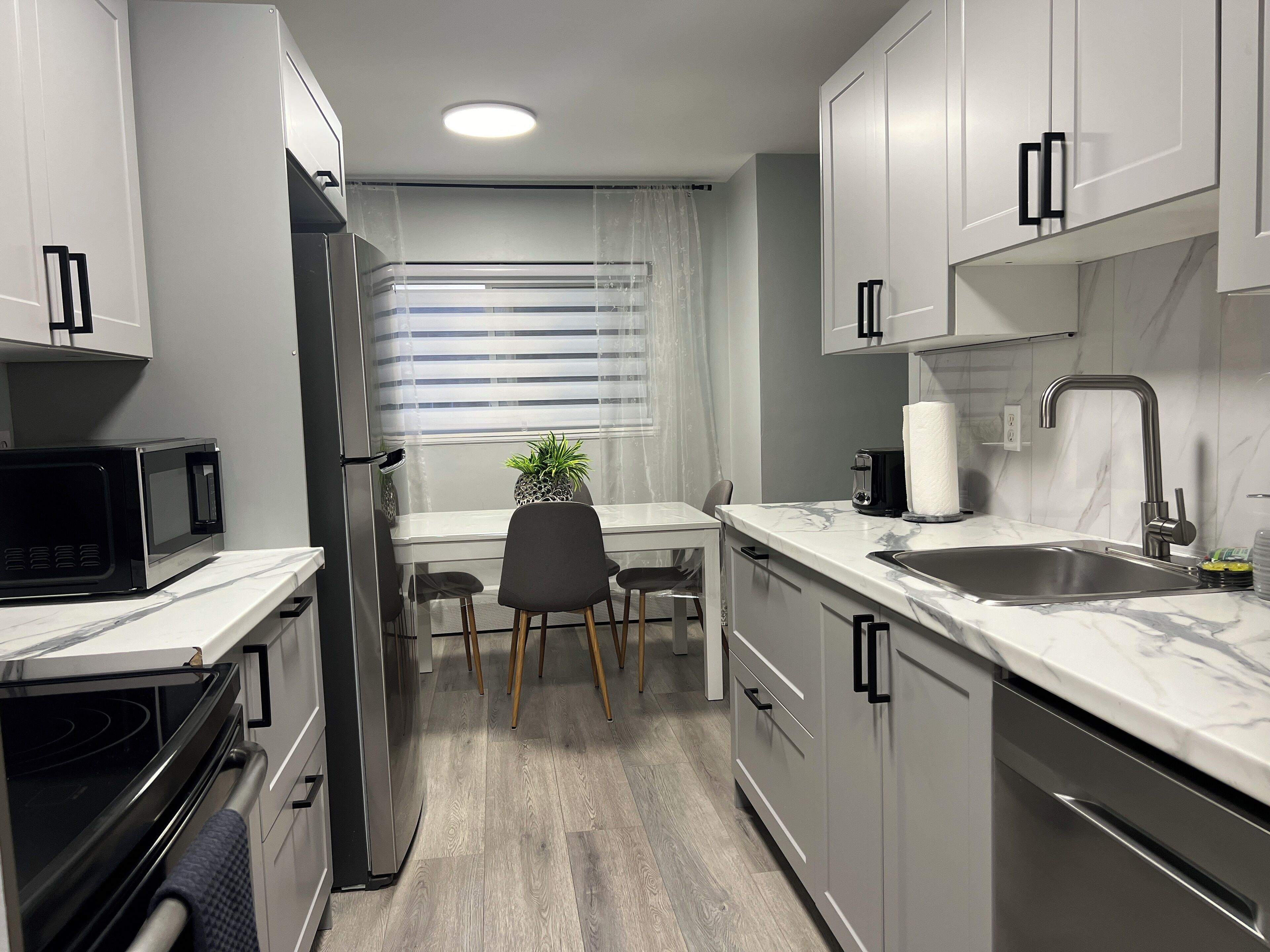 A compact kitchen with white cabinets, a built-in oven, a microwave, a sink, and a window with blinds.