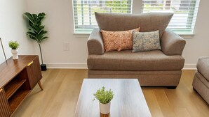 A modern living room with a wooden coffee table, a sofa, and a potted plant. - Cozy & Chic - Worker Friendly w/ Gym Pool & Lndry (Sherman)