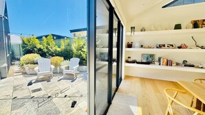 Un intérieur moderne avec une porte vitrée donnant sur un patio aménagé avec des meubles d’extérieur et des plantes.