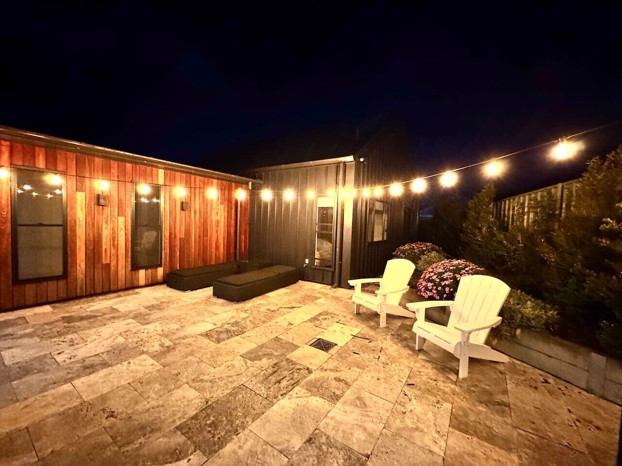 A patio with stone flooring, wooden walls, and white chairs.