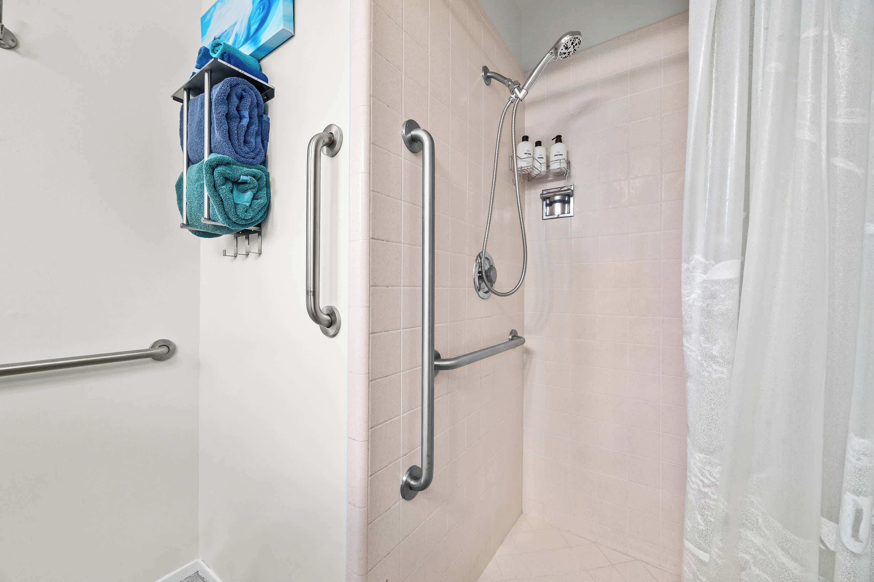 A shower with a handheld showerhead, grab bars, and a towel rack with towels.