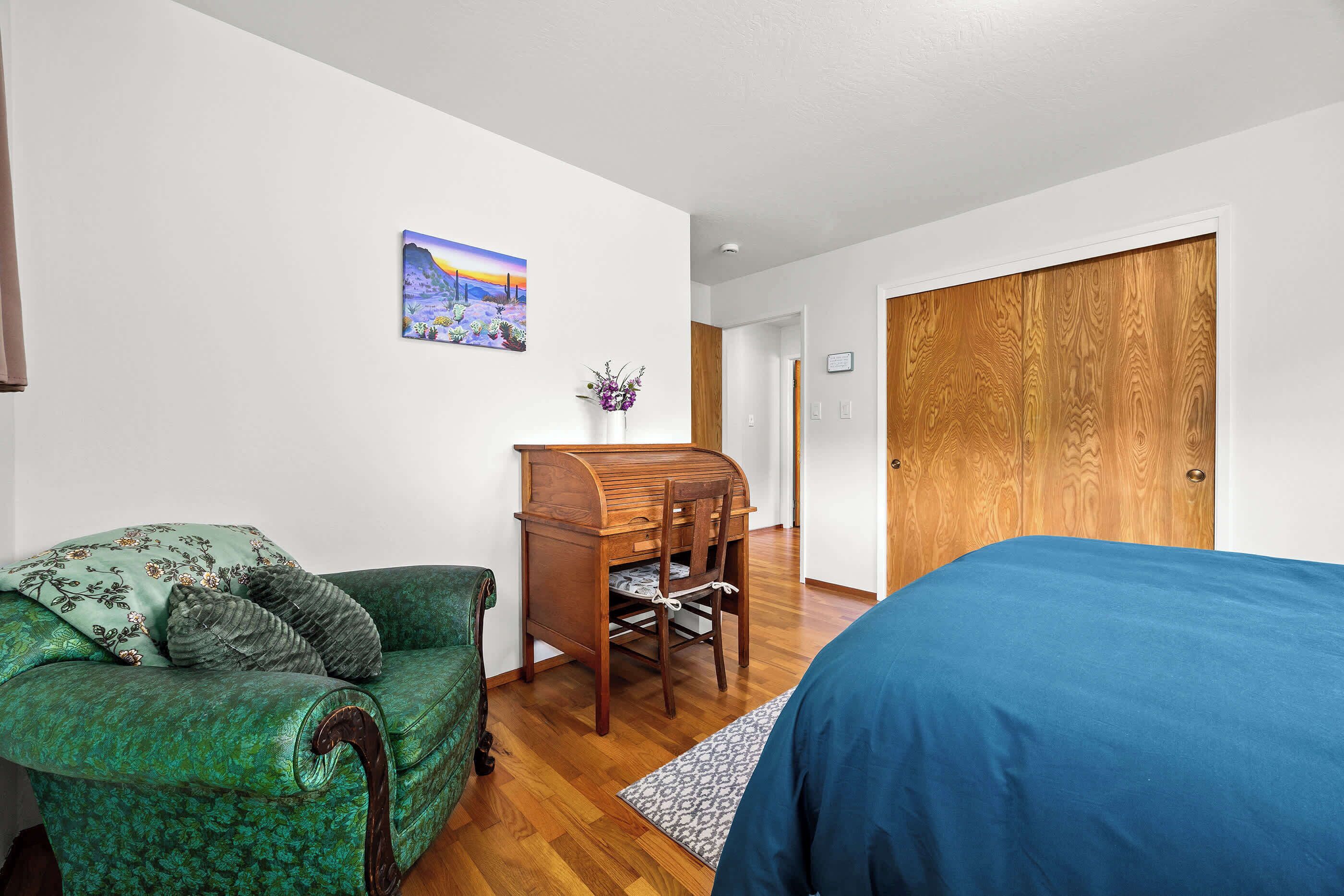 Une chambre à coucher avec un canapé à motifs verts, un bureau en bois, un lit bleu et une armoire en bois.