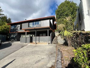 Et moderne hus med to etager og en stentrappe, der fører op til indgangen, omgivet af grønt og en blå himmel.