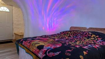 Una habitación con una cama cubierta por un edredón de colores, una puerta blanca y una pared con un efecto de luz púrpura.